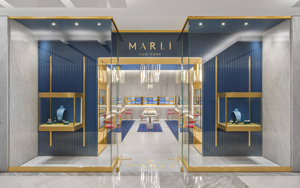 A storefront with glass windows and jewelry displays. There is marble floors with navy blue walls and gold accents.