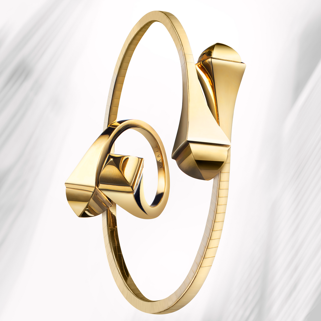 A solid yellow gold bracelet and ring on top of a blurred background. 