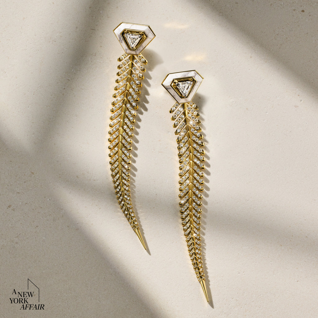 Gold earrings with leaf-like design on a beige background