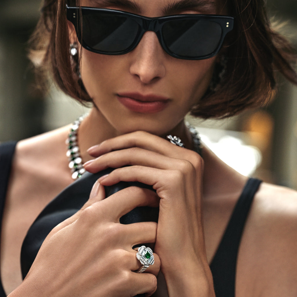 Woman wearing black sunglasses and a black top with a close-up of her hand holding a necklace.