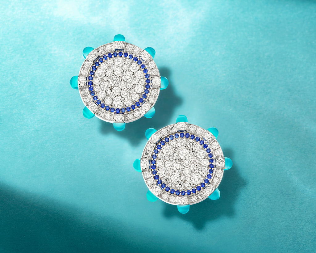 Pair of round earrings with blue and white gemstones on a teal background