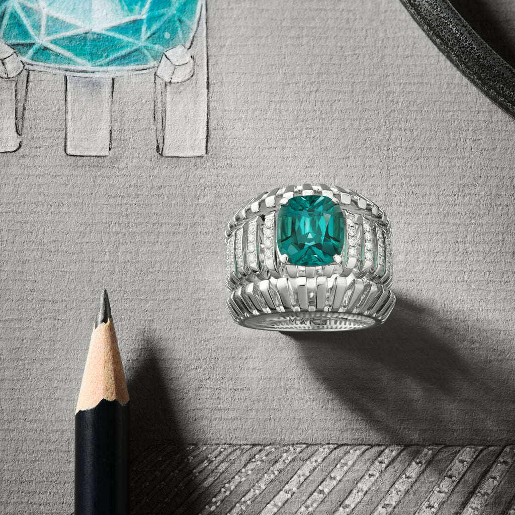 Silver ring with a green gemstone on a gray surface with a pencil and drawing.