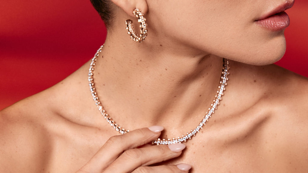 A close up of a woman's chin and bare shoulders, while she is touching a diamond necklace