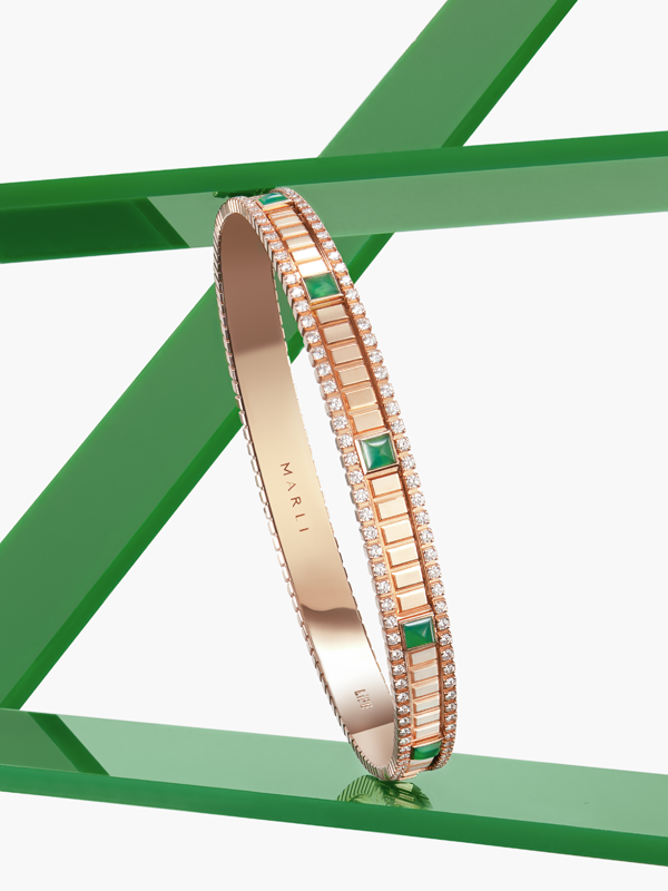 A rose gold bracelet with green agate gemstones and diamonds. It's sitting diagonally on green shiny bars. 